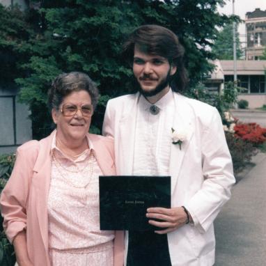 young man stands with college diploma and senior woman