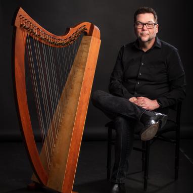 man seated next to folk harp