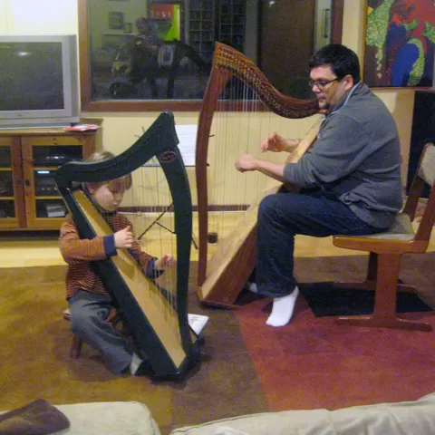 a man and a boy sit behind harps facing each other.
